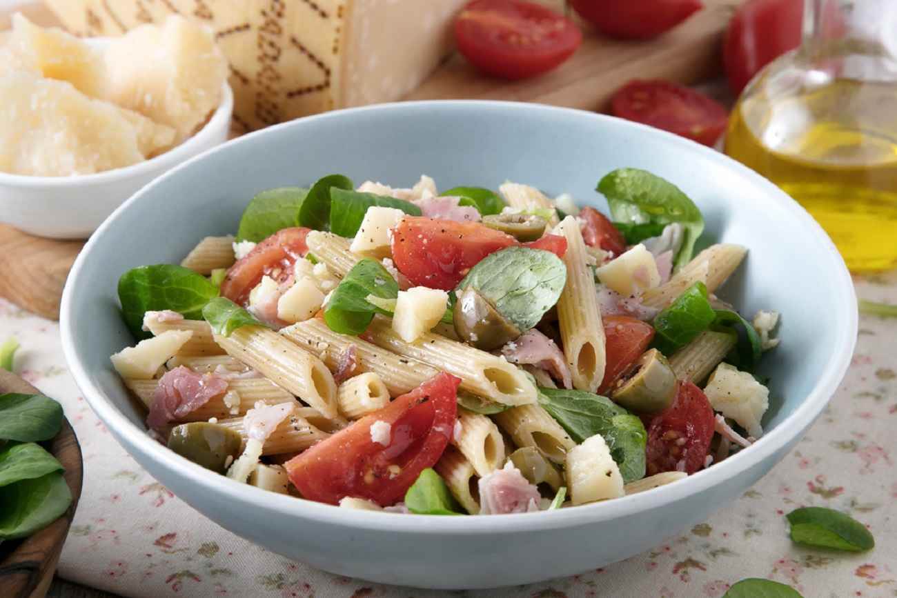 Kalter Nudelsalat mit Tomaten, grünen Oliven, Kochschinken, Feldsalat und Grana Padano