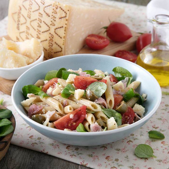Cold pasta salad with cherry tomatoes, green olives, ham, lamb’s lettuce and Grana Padano