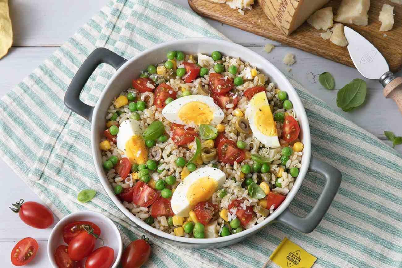 Brown rice salad with peas, tomatoes, hard-boiled eggs, green olives, corn, basil and Grana Padano PDO