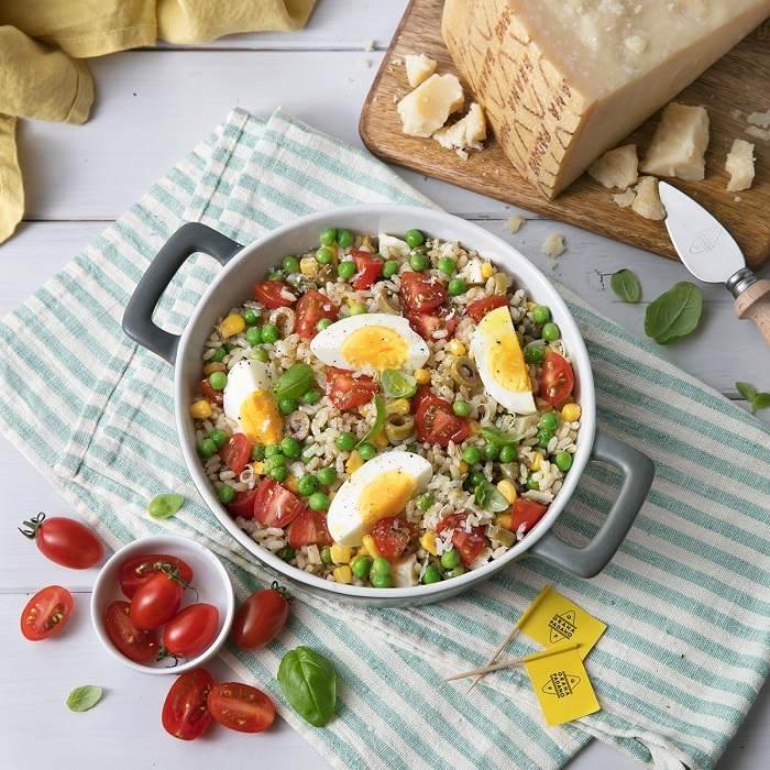 Brown rice salad with peas, tomatoes, hard-boiled eggs, green olives, corn, basil and Grana Padano PDO