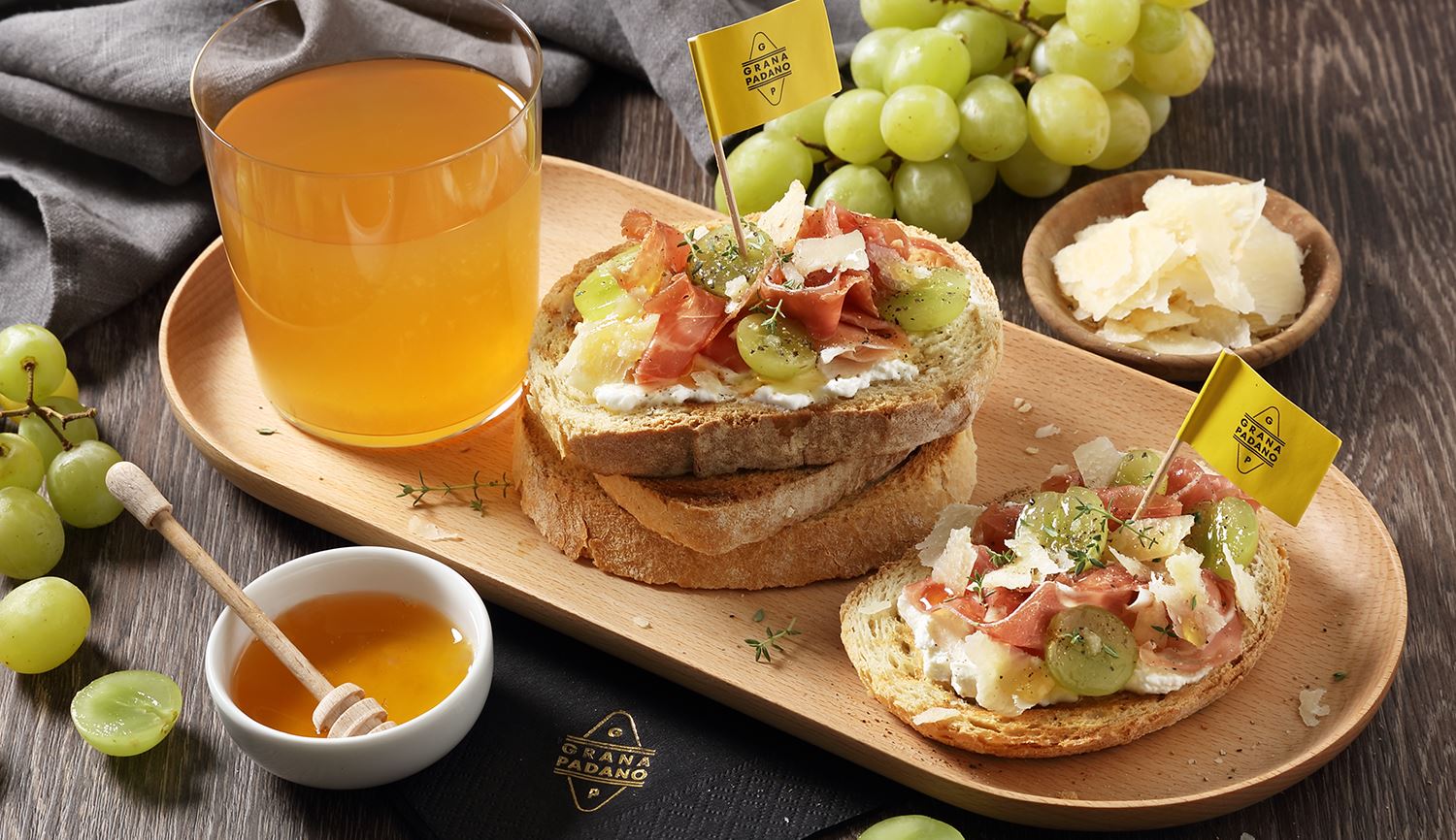 Apfel-Cidre und hausgemachte Brot-Tarteletts mit weißen Trauben, rohem Schinken, Honig und gehobeltem Grana Padano 